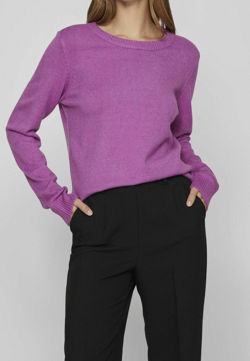 Livfull lila tröja med rundad halsringning och ribbade manschetter, matchad med skräddarsydda svarta byxor. Slät struktur, klassisk passform.