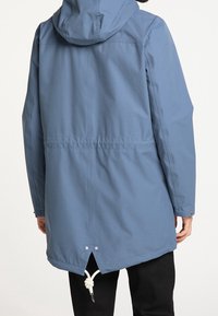 Ljusblå vattentät jacka med huva, dragsko i midjan, ventilationsöppning i ryggen och tryckknappar. Slät textur, medellång design.