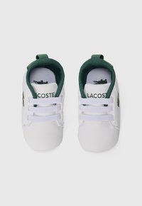 Scarpe bianche stringate con accenti verdi, caratterizzate da una texture liscia e un piccolo logo Lacoste sul lato e sul tallone.