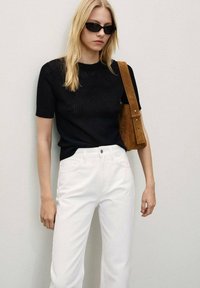 Maglietta nera a maniche corte in maglia abbinata a pantaloni bianchi a vita alta e una borsa a tracolla in suede marrone. Gli occhiali da sole completano il look.