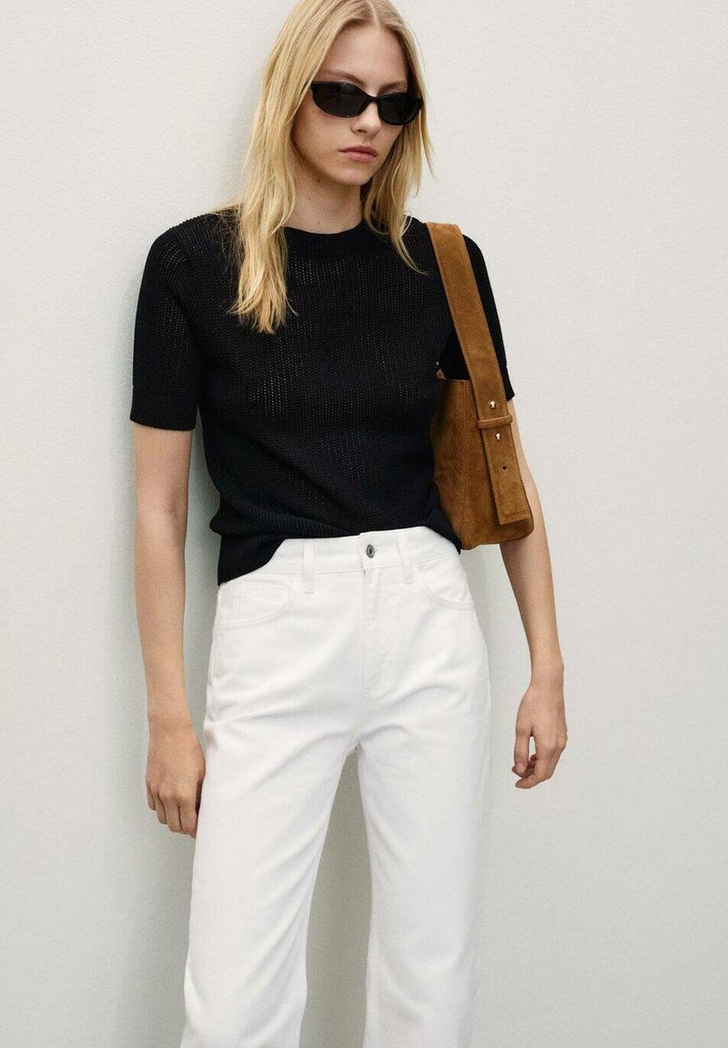 Maglietta nera a maniche corte in maglia abbinata a pantaloni bianchi a vita alta e una borsa a tracolla in suede marrone. Gli occhiali da sole completano il look.