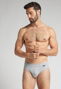 Szare bawełniane slipy z miękkim pasem i detalami szwów, na neutralnym tle. Model bez koszulki, ukazujący muskularną sylwetkę.