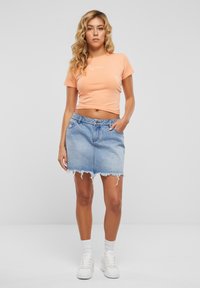 Barack rövid ujjú crop top fehér grafikával, világoskék farmer szoknyával párosítva, melynek szegélye rojtos és elülső zsebe van. Fehér sportcipő.