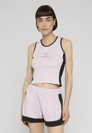 Nainen, jolla on lyhyet tummat hiukset ja päällään hihaton vaaleanpunainen ja musta crop top sekä yhteen sopivat shortsit, joissa on merkkilogot molemmissa vaatekappaleissa.