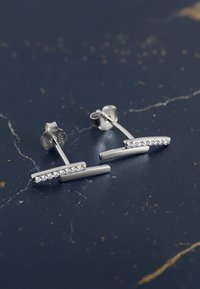 Orecchini d'argento con un design a barra dritta, caratterizzati da piccole pietre preziose trasparenti incastonate lungo un bordo, texture liscia e chiusura a perno.