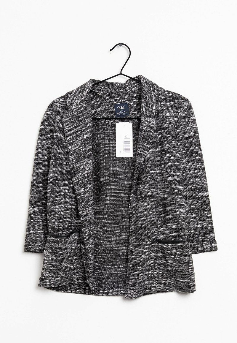 Blazer texturé noir et blanc avec un col châle, ouvert à l'avant et deux poches avant, suspendu à un crochet noir. Étiquette visible à l'intérieur.