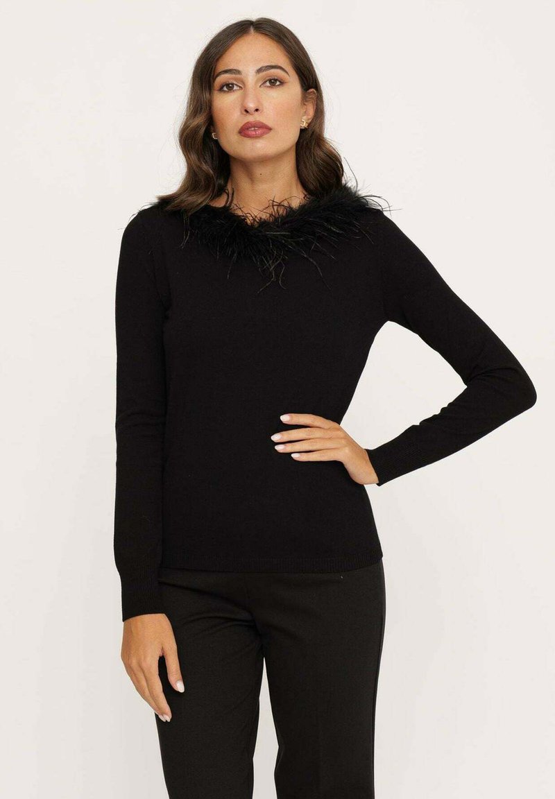 Zwarte trui met een tekstuele zwarte veren kraag. Lange mouwen en een getailleerd ontwerp. Gedragen met zwarte broek.