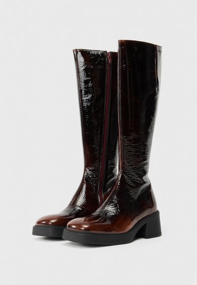 Καφέ, γυαλιστερά μποτάκια μέχρι το γόνατο με υφή, στρογγυλή μύτη και τετράγωνη φτέρνα. Διαθέτουν ορατό φερμουάρ στο πλάι με αντίθετη λαβή.