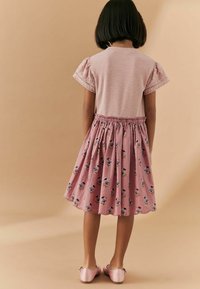 Rosa klänning med broderade blommönster, randig topp, vågig nederkant och korta ärmar med spetskant. Matchad med rosa skor.