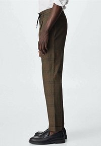 Brązowe spodnie w kratę z elastycznym paskiem ze sznurkiem, zwężanym nogawkami i czarnymi mokasynami; wzór ozdobiony pomarańczowymi akcentami.