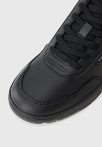 Baskets en cuir noir avec un bout arrondi, des détails perforés, des lacets plats noirs et une semelle texturée avec un marquage minimal.