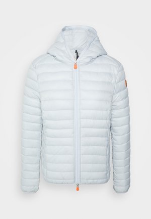 Chaqueta acolchada de color gris claro con capucha, cremallera frontal con pestañas naranjas y un pequeño parche redondo en la manga izquierda.