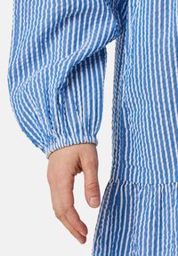 Blue and white striped dress with long, gathered sleeves, textured fabric, and a tiered skirt design. Close-up on sleeve and hand.