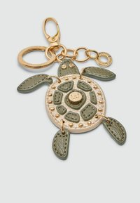 Portachiavi a forma di tartaruga realizzato in pelle verde testurizzata con accenti dorati e borchie. Presenta un gancio per l'attacco e link decorativi.