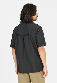 Zwart kortemouwshirt met een losse pasvorm en een klepdetail over de schouders, van achteraf weergegeven. Soepele textuur en eenvoudig ontwerp.