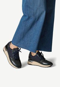 Sneaker neri e blu con tomaia texturizzata, chiusura con lacci e suola beige. Gli accenti dettagliati mettono in evidenza il design sportivo. Abbinati a pantaloni in denim larghi.