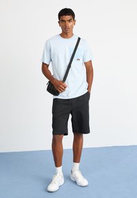 Lys blå stripete t-skjorte med lomme, svarte shorts og hvite joggesko. T-skjorten har en liten logo på lommen.