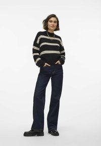 Maglione a righe nere e crema con scollo rotondo, abbinato a jeans ampi blu scuro e scarpe chunky nere. Materiale a maglia texturizzato.