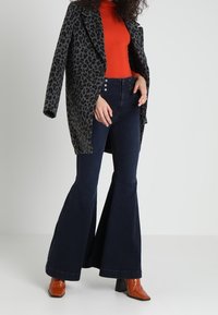 Rozšířené tmavě modré džíny doplněné šedým kabátem s zvířecím potiskem a slušivým červeným rolákem, doplněné hnědými botami na podpatku.