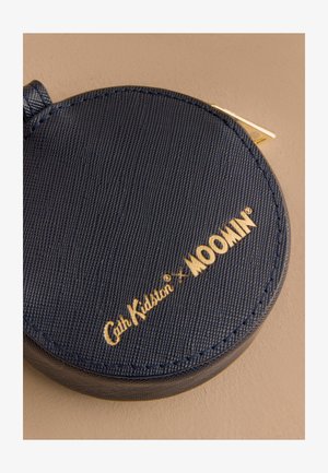 Apaļa tumši zilas ādas monētu maciņš ar teksturētu apdari, kam ir zeltā izsistis logo "Cath Kidston x MOOMIN" un metāla rāvējslēdzējs.