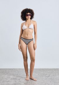 Bikini-set med en lysfarget trekantet topp og svart-hvite stripete høyhåndte truser. Modell med mørke solbriller.