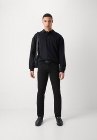 Polo negro de manga larga con cuello abotonado, combinado con jeans negros ajustados y zapatos negros. Diseño sencillo sin patrones.
