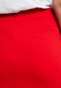 Jupe ajustée rouge en tissu lisse et extensible avec une texture subtile. Présente un design épuré et une couture centrale qui descend à l'avant.