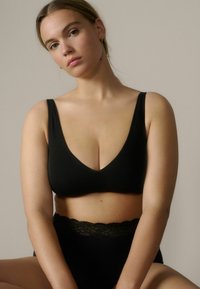 Conjunto de lencería de tela negra que incluye un bralette con escote en V profundo y braguitas de talle alto con un borde de encaje, colocado sobre un fondo neutro.