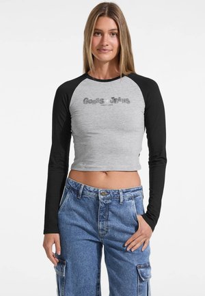 Gray cropped long-sleeve shirt with black raglan sleeves, featuring a silver Guess Jeans logo on the front. Casual fit and smooth texture.