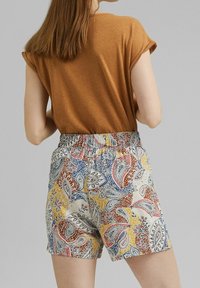 Top marrón de mangas remangadas combinado con pantalones cortos de colores con estampados de cachemira en azul, rojo, amarillo y blanco, con una cintura elástica.