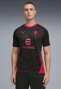 Sort og rød fodboldtrøje med korte ærmer. Har et struktureret mønster, rund krave og Puma-logoet på venstre bryst.