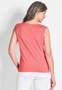 Mouwloos koraalkleurig topje met een gladde textuur, ronde halslijn en een licht taps toelopende pasvorm, gecombineerd met witte broek.