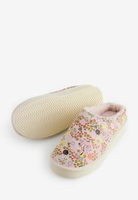 Een paar instap slippers met een bloemenpatroon, een fuzzy roze binnenvoering en een rubberen zool met zigzagprofiel, weergegeven op een witte achtergrond.