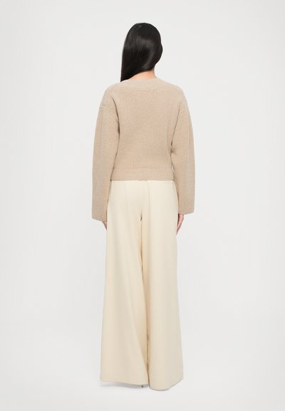 Maglione a coste beige con scollatura rotonda, abbinato a pantaloni larghi crema a vita alta, mostrato da dietro.