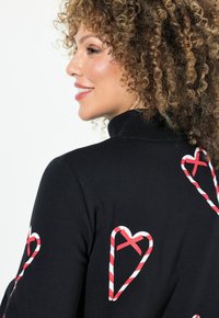 Maglione nero con motivi a forma di cuore a bastoncini di zucchero rossi e bianchi, colletto alto e design aderente. Tessuto morbido e stile informale.