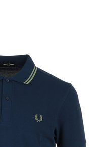 Camisa polo azul marino con cuello bicolor de rayas verdes, dos botones y un pequeño logo bordado en verde en el lado izquierdo del pecho.