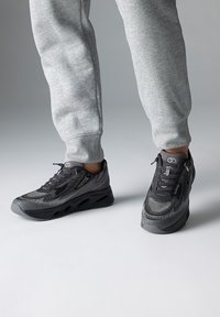 Chaussures de sport noires et grises avec une tige en maille, un motif texturé et une semelle arrondie dotée d'ouvertures de ventilation. Design à lacets.