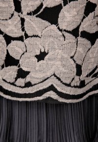 Svart nättyg med stora vita blomsterbroderier över plisserat svart material under.