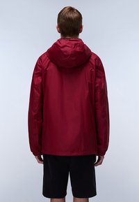 Rode, lichtgewicht jas met een capuchon, gladde textuur en lange mouwen, van achteren getoond, gecombineerd met zwarte shorts.