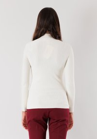Top bianco a maniche lunghe a coste con un colletto alto e design aderente, abbinato a pantaloni bordeaux con un leggero apertura sul retro.