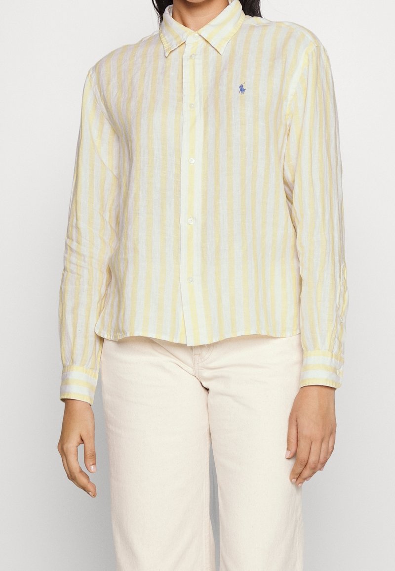Linen shirt featuring vertical yellow and white stripes, button-down collar, and small blue logo. Long sleeves with buttoned cuffs.