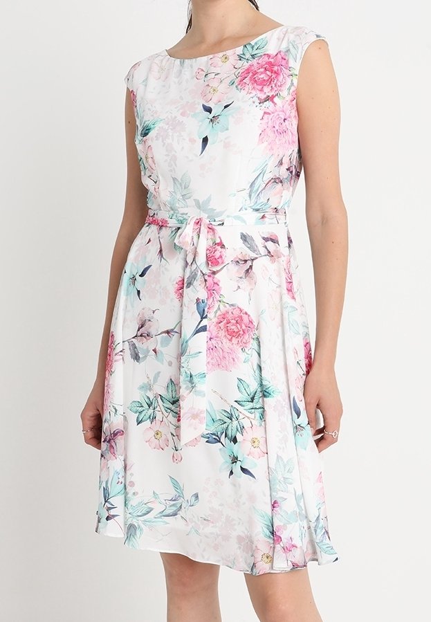Blommig klänning gjord av lätt tyg, med ärmlös design, rund halsringning och en knytbälte. Färgerna inkluderar vitt, rosa och teal.