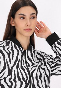 Bomber jacket se zebřími pruhy v černé a bílé, s předním zipem, žebrovaným límcem a manžetami, a hladkým povrchem.