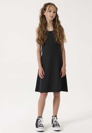 Schwarzes ärmelloses Kleid mit taillierter Oberseite und weitem Rock, kombiniert mit schwarzen High-Top-Sneakern mit weißen Schnürsenkeln.