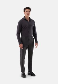 Camicia grigia scuro a maniche lunghe, con bottoni, abbinata a pantaloni tailored grigio antracite. Scarpe in pelle nere completano l'outfit formale.