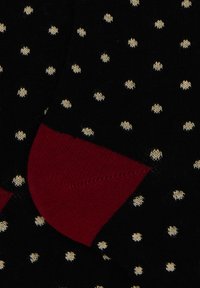 Black socks with white polka dots and contrasting solid red heel detail, close-up view of fabric texture and knit pattern.