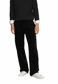 Mustat samettihousut rentoa mallia, joissa on etutaskut ja sileä pinta. Yhdistetty valkoisiin lenkkareihin ja mustaan pitkähihaiseen paitaan.