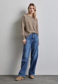 Beiger Strickpullover mit gerippten Bündchen, kombiniert mit hellblauen weit geschnittenen Jeans und beigen Slippern. Schlichtes Design mit lässiger Passform.