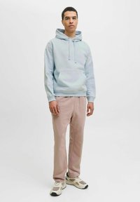 Sudadera azul claro con cordones y bolsillo frontal, combinada con pantalones de chándal rosa suave. Usada con zapatillas beiges y grises. Diseño simple.