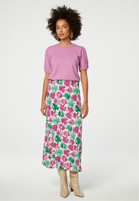 Lavendel top met puffmouwen gecombineerd met een lange rok met een bloemenpatroon in roze en groen, gedragen met beige knielange laarzen.